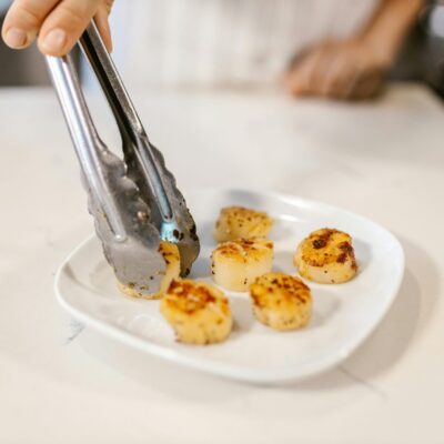 Close-up of grilled scallops served on a plate with metal tongs indoors.